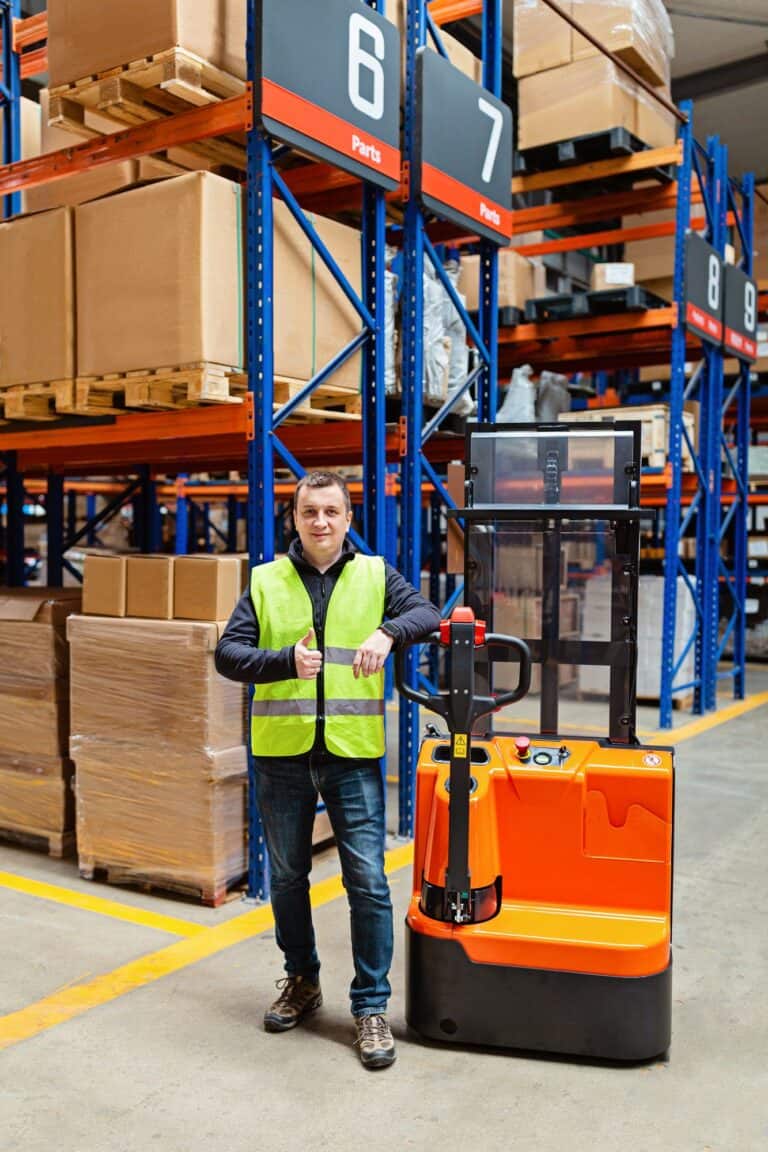 Worker in uniform standing on modern warehouse with shelves and reach truck