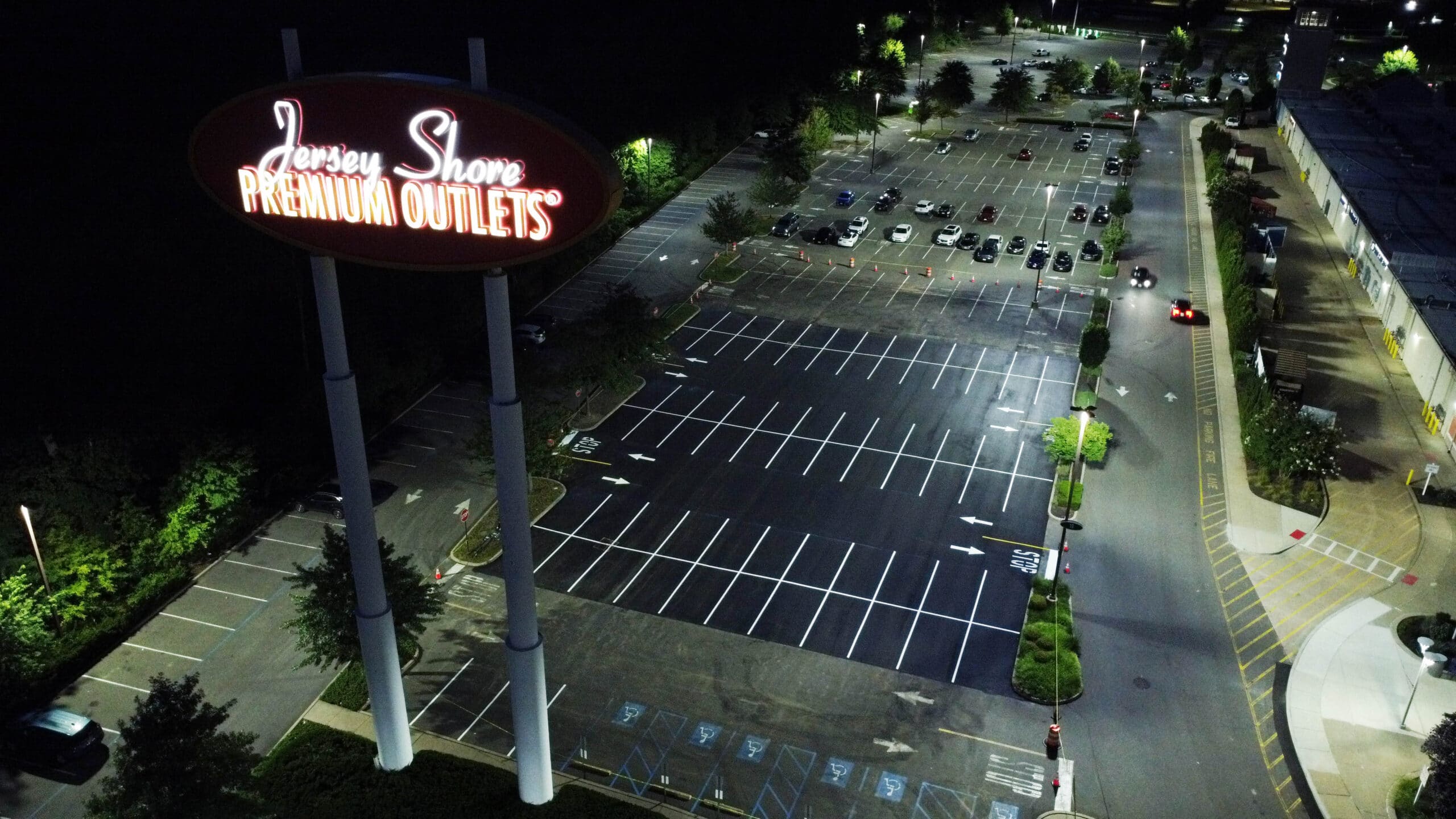 Nighttime aerial view of freshly repaved and restriped parking lot at Jersey Shore Premium Outlets, Tinton Falls, NJ, with bright white line markings.