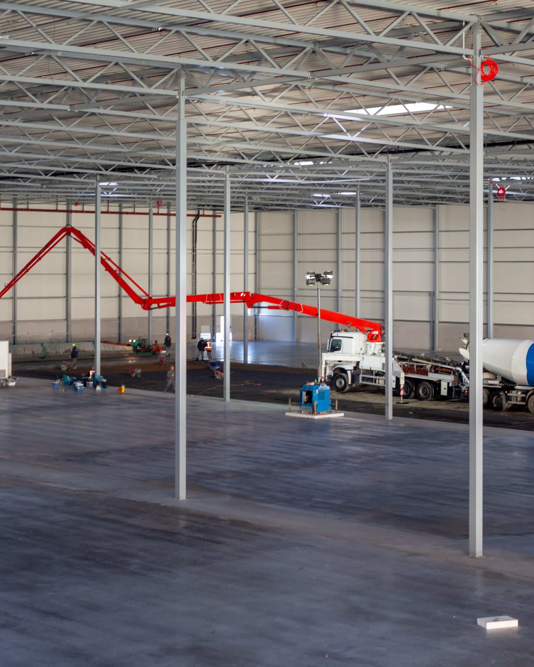 Crew and concrete mixer working on large warehouse floor during surface preparation.