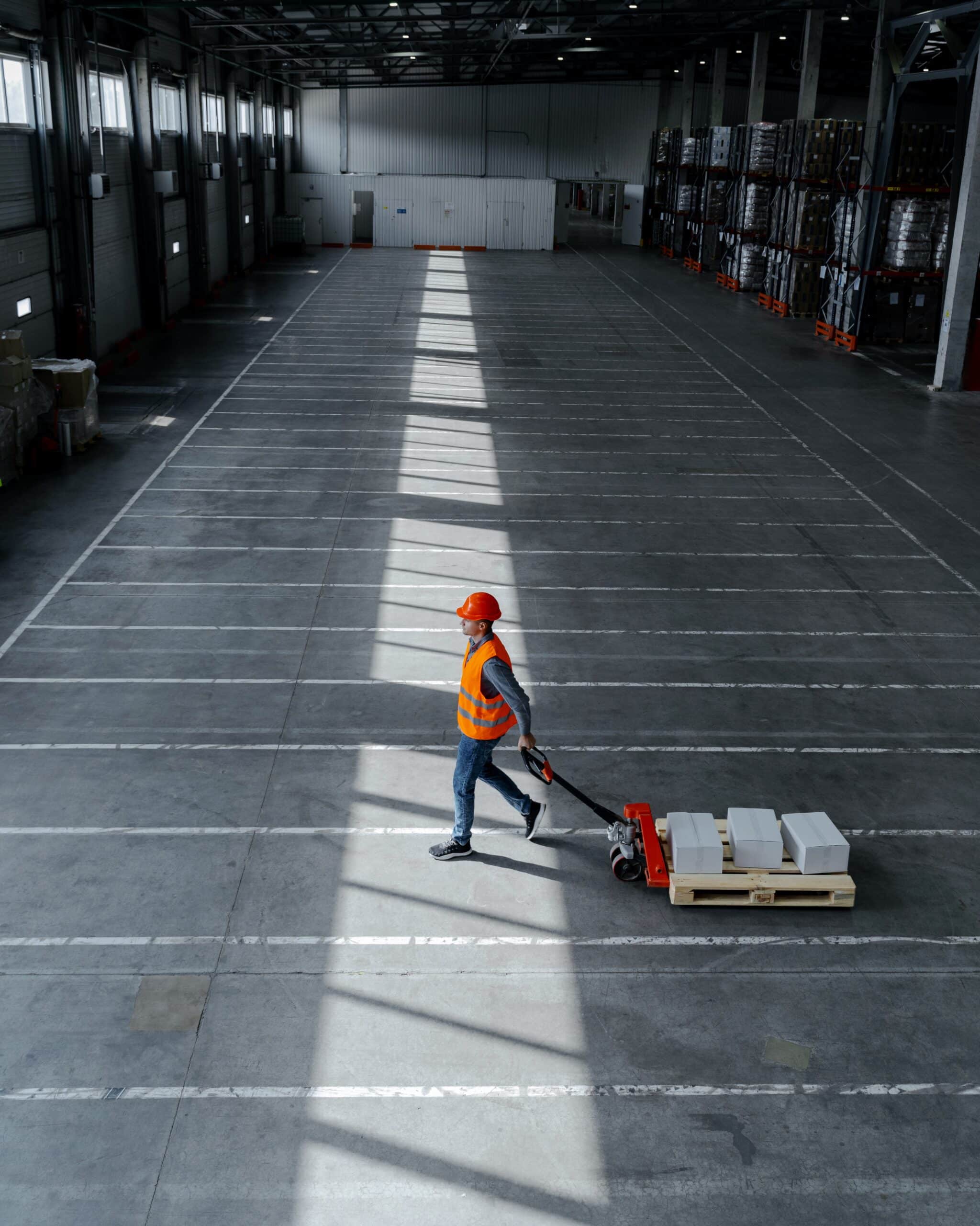 Worker in safety vest walking across warehouse floor with old painted lines ready for re-striping.