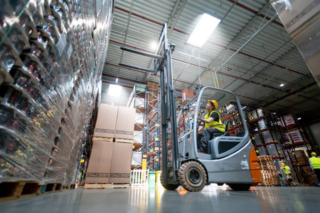 Forklift operator moving pallets in an active warehouse with clean concrete flooring and clear traffic areas.