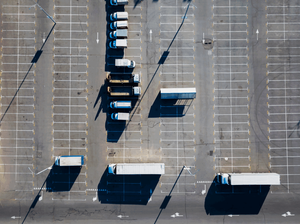 Aerial view of a commercial parking lot with trucks, marked lanes, and visible pavement wear.