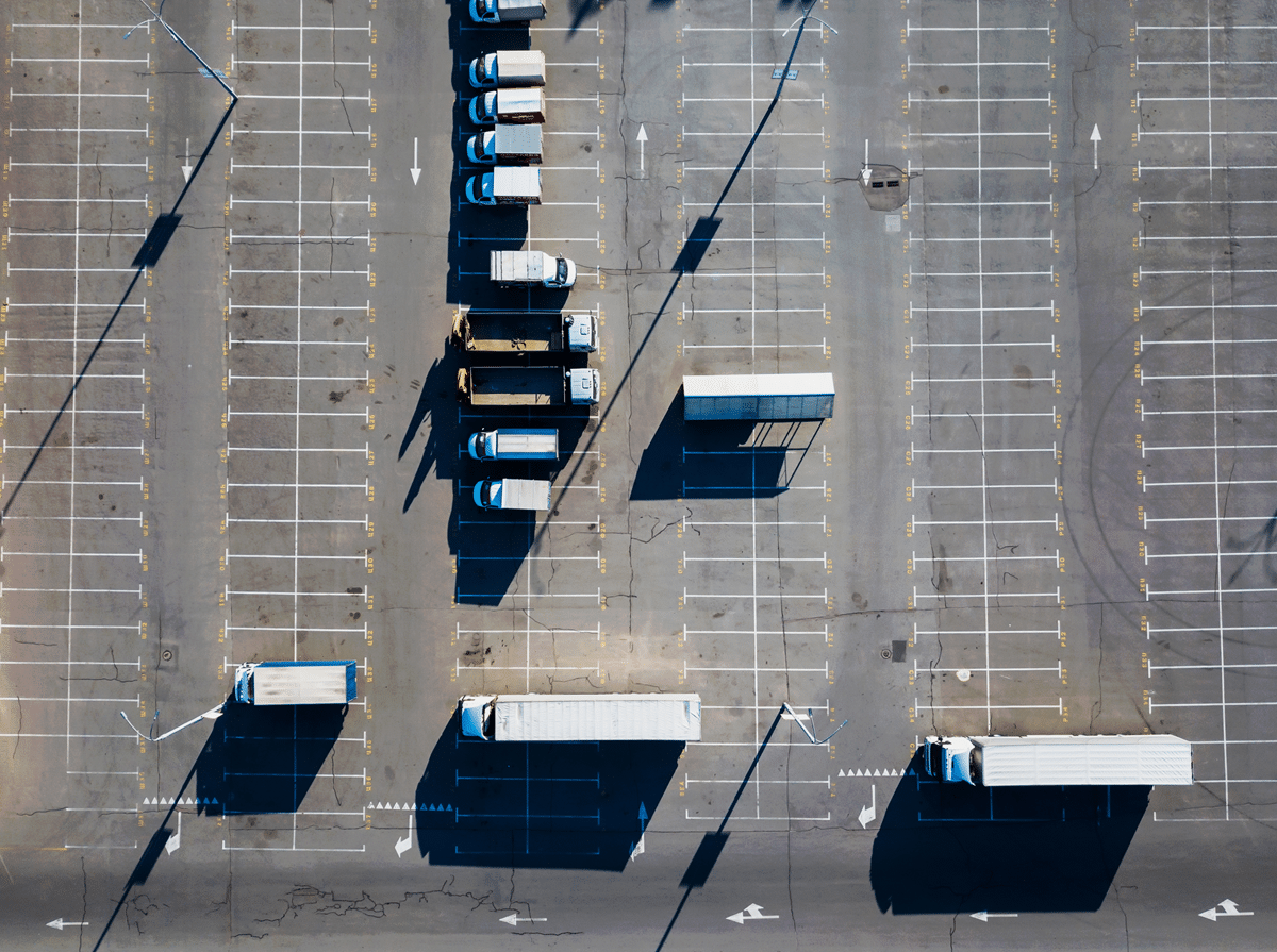Aerial view of a commercial parking lot with trucks, marked lanes, and visible pavement wear.