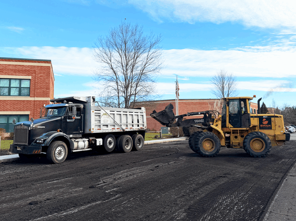 Asphalt milling and site preparation with loader and dump truck before paving begins.