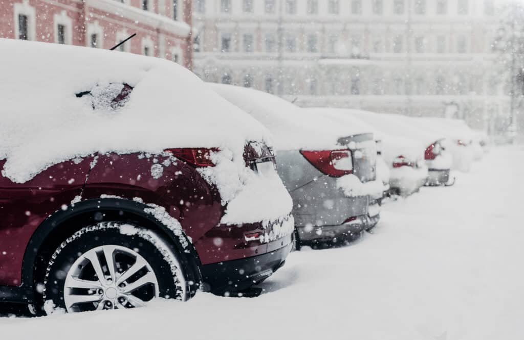 Snow-covered cars in a parking lot during winter, with pavement conditions hidden beneath.