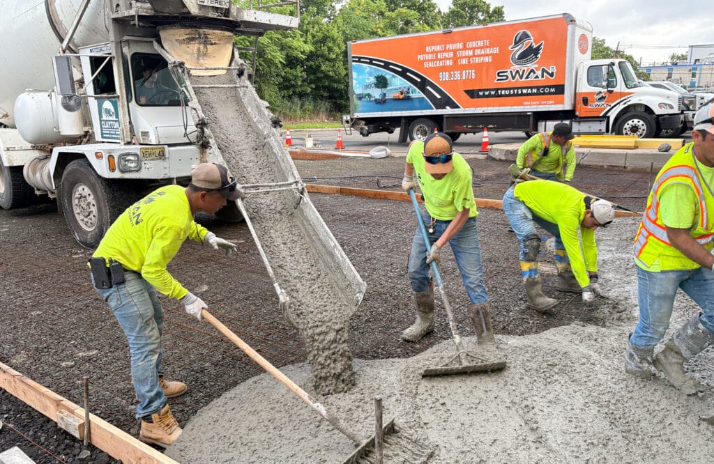 Concrete being poured by crew at commercial site, showing paving material installation process.